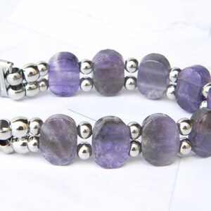 Puede incluir: Una pulsera con cuentas ovaladas de amatista p&uacute;rpura intercaladas con peque&ntilde;as cuentas plateadas. La pulsera tiene un cierre plateado. Las cuentas de amatista son transl&uacute;cidas.