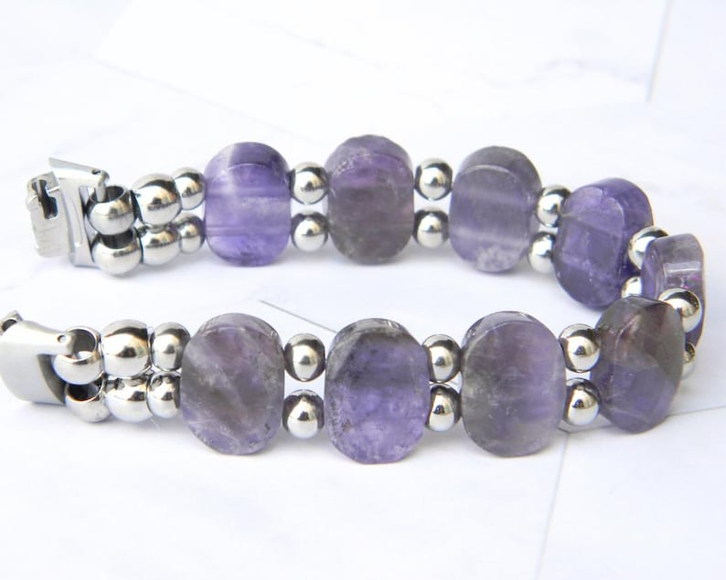 Puede incluir: Una pulsera con cuentas ovaladas de amatista p&uacute;rpura intercaladas con peque&ntilde;as cuentas plateadas. La pulsera tiene un cierre plateado. Las cuentas de amatista son transl&uacute;cidas.