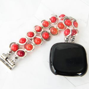 May include: A red and orange beaded watch band with a silver clasp. The band is made of two rows of beads, and the beads are graduated in size. The band is attached to a black watch face.