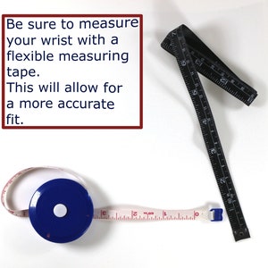Op de afbeelding: Twee meetlinten, een zwart en een wit met een blauwe behuizing. Het zwarte lint is 45,7 cm lang en het witte lint is 30,5 cm lang. De tekst op de afbeelding luidt: "Zorg ervoor dat je je pols meet met een flexibel meetlint. Dit zorgt voor een nauwkeurigere pasvorm."
