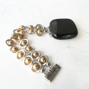 May include: A gold and silver beaded watch band with a black watch face. The band is made of small gold beads and silver links.