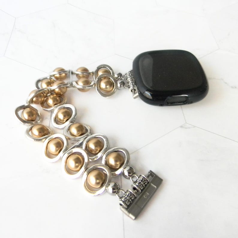 May include: A gold and silver beaded watch band with a black watch face. The band is made of small gold beads and silver links.