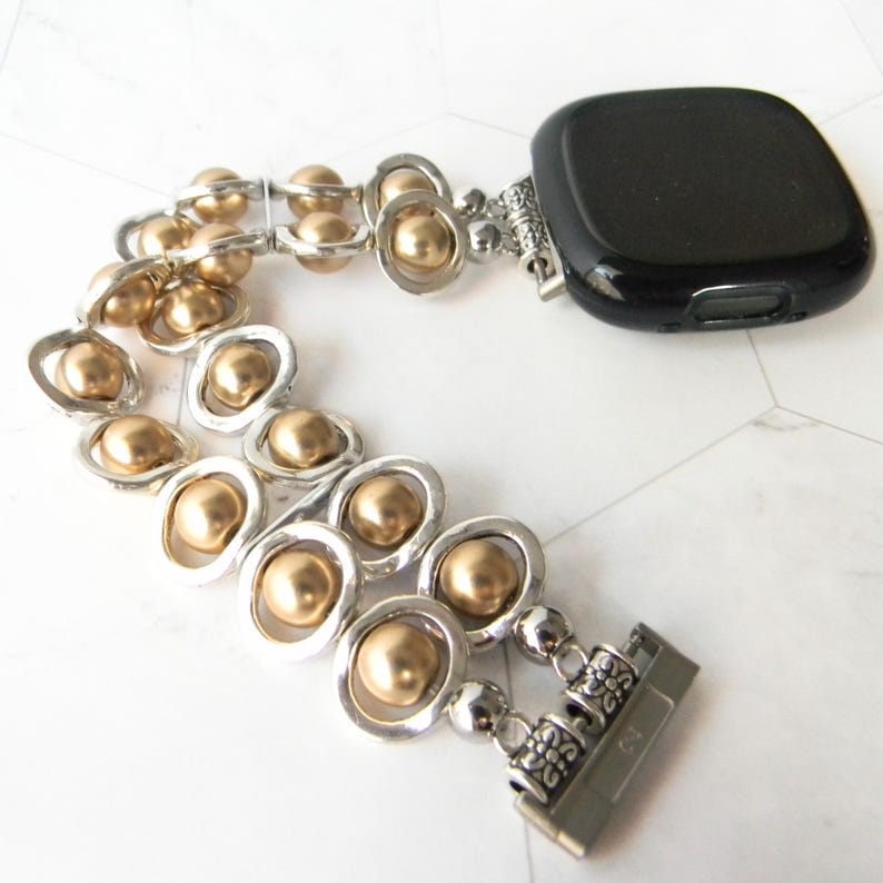 May include: A gold and silver beaded watch band with a black watch face. The band is made of small gold beads and silver rings.