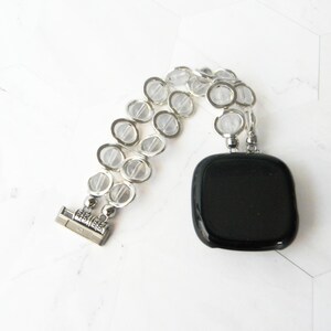 May include: A silver bracelet with clear glass beads and a black square pendant.