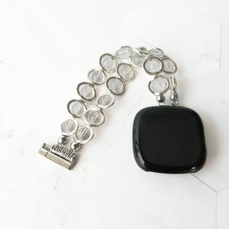 May include: A silver bracelet with clear glass beads and a black square pendant.