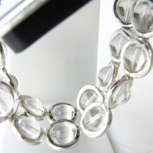 May include: A silver bracelet with clear crystal beads. The beads are round and have a faceted design. The bracelet is made of two rows of beads.
