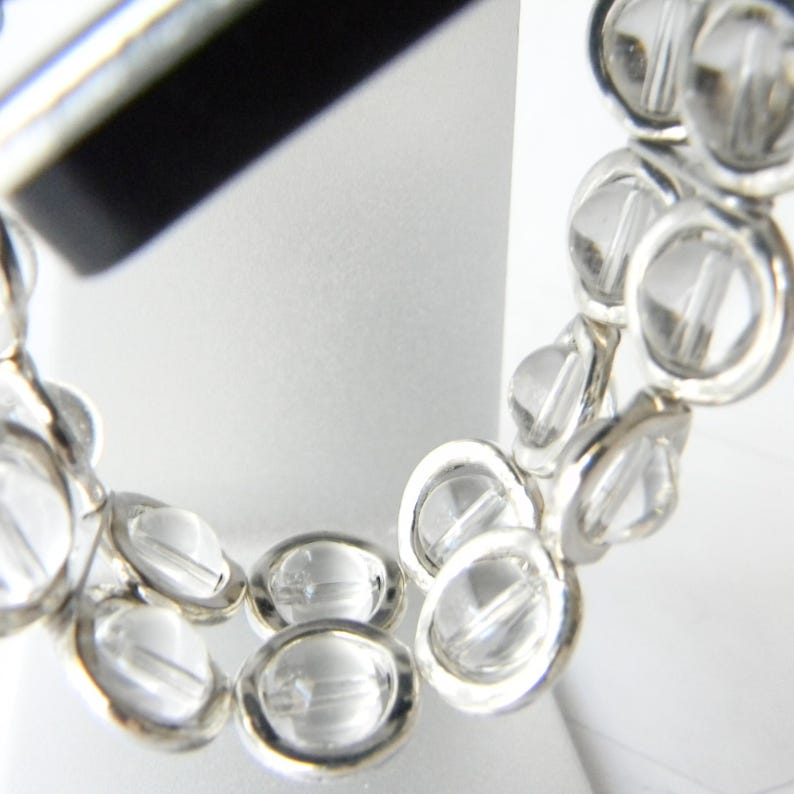 May include: A silver bracelet with clear crystal beads. The beads are round and have a faceted design. The bracelet is made of two rows of beads.