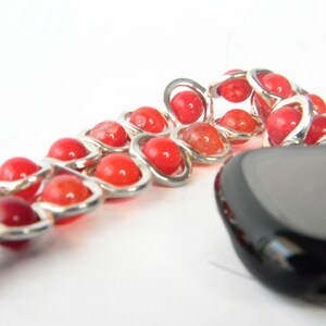 May include: A red and silver beaded bracelet with a black stone charm. The beads are round and have a smooth, polished finish. The bracelet is made of metal and has a chain-like design.