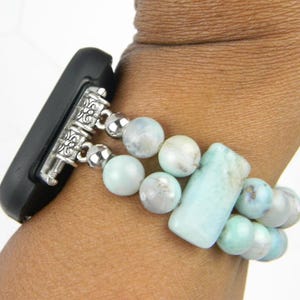 May include: A light blue and white beaded watch band with silver accents. The band is made of round and rectangular beads.