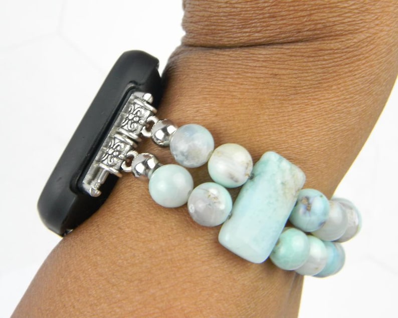May include: A light blue and white beaded watch band with silver accents. The band is made of round and rectangular beads.