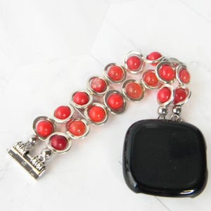 May include: A silver and red beaded watch band with a black watch face. The band is made of small, round beads with a silver metal ring around each bead. The beads are a gradient of red, with the darkest red beads at the bottom and the lightest red beads at the top.