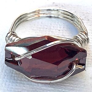 May include: A silver wire wrapped ring with a dark red faceted gemstone.