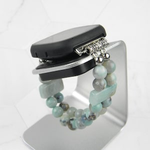 May include: A smartwatch with a black band and a beaded bracelet with light blue and green stones. The bracelet has silver accents.