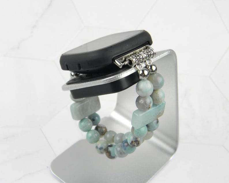 May include: A smartwatch with a black band and a beaded bracelet with light blue and green stones. The bracelet has silver accents.