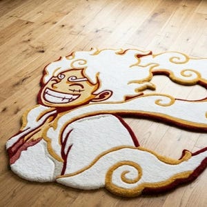 Op de afbeelding: Een op maat gemaakte vloerkleed met een lachend stripfiguur met witte, gele en rode accenten. Het vloerkleed heeft een wolkvorm en ligt op een houten vloer.