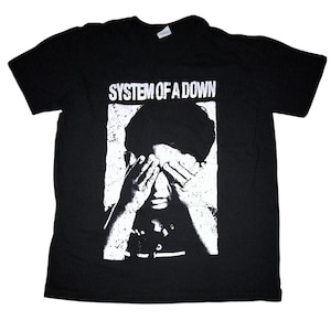 Może przedstawiać: Czarny t-shirt z nazwą zespołu "SYSTEM OF A DOWN" w białym kolorze nad czarno-białą grafiką osoby zasłaniającej oczy. Koszulka ma okrągły dekolt.