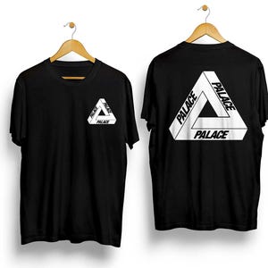 Puede incluir: Dos camisetas negras con la palabra "PALACE" en blanco, formando un dise&ntilde;o triangular. Una camiseta tiene el logo en el pecho, la otra en la espalda. Ambas cuelgan de perchas de madera.