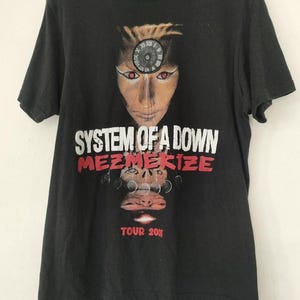 May include: Black t-shirt with a graphic of a face with a clock on the forehead and the band name "SYSTEM OF A DOWN" in white. The word "MEZMERIZE" is in red, and "TOUR 2005" is at the bottom.