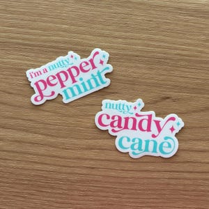 May include: Two white stickers with pink and teal text on a wooden surface. One sticker reads "I'm a nutty peppermint" and the other reads "nutty candy cane". Both stickers have a decorative design.