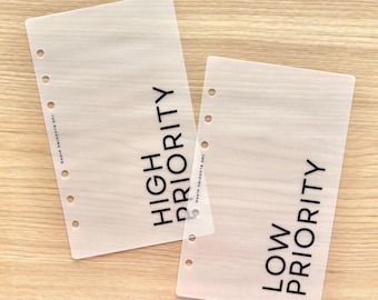 May include: Two translucent, frosted planner dashboard inserts with six punched holes along the left edge. One sheet features the black text HIGH PRIORITY, and the other features LOW PRIORITY. Both include the small text THE BLUSHING HIPPO.