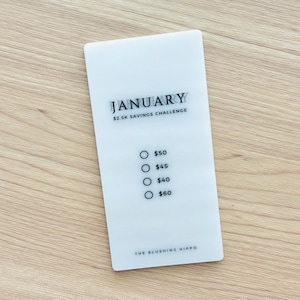 May include: A white card with the text "JANUARY $2.5K SAVINGS CHALLENGE" and a list of dollar amounts with radio buttons: $50, $45, $40, $60. The bottom of the card reads "THE BLUSHING HIPPO".