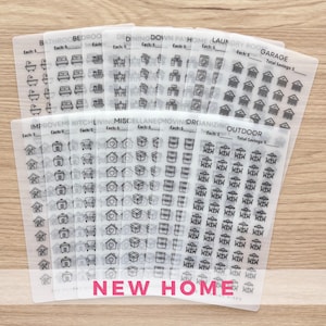 May include: A collection of clear, transparent stickers with black line art illustrations of household items and rooms. The stickers are labeled with room names like "Bathroom," "Bedroom," and "Garage." The text "NEW HOME" is printed in pink at the bottom.