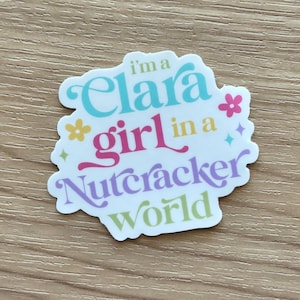 May include: A white sticker with the text "I'm a Clara girl in a Nutcracker world" in various colors. The sticker has a floral and star design.