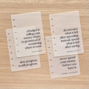 May include: Four translucent, rectangular planner inserts with six punched holes along the left edge. Each insert features black printed text: quotes by Dave Ramsey, Warren Buffett, Thomas Jefferson, and the phrase slow progress is still progress.