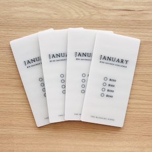 May include: Four white cards with the word "January" and different savings challenge amounts. The cards have circles for marking progress. The card on the right has the text "January $10K Savings Challenge" and lists amounts to save: $250, $160, $200, and $240.
