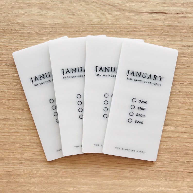 May include: Four white cards with the word "January" and different savings challenge amounts. The cards have circles for marking progress. The card on the right has the text "January $10K Savings Challenge" and lists amounts to save: $250, $160, $200, and $240.