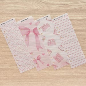 May include: Four planner dividers with pink designs and text. The dividers include the phrases "High Priority", "Savings", "Low Priority", and "Month Ahead". The designs include bows, hearts, and gift boxes. Each divider has multiple holes for binding.