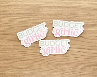 May include: Three die-cut stickers featuring the text BUDGET in a sage green sans-serif font and girlie in a pink cursive script. Each sticker includes small four-pointed star accents surrounding the text on a white background.