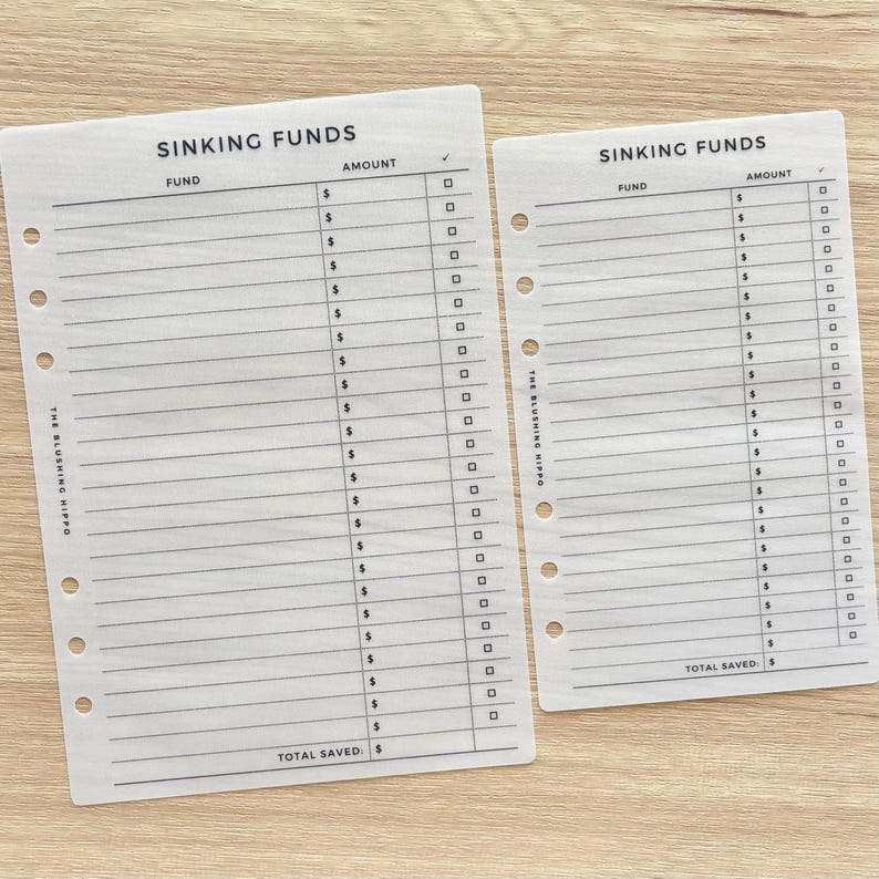 May include: Two white paper planner inserts for tracking sinking funds, featuring black printed text and lines. Each sheet includes columns for fund names, dollar amounts, and checkboxes, with the text THE BLUSHING HIPPO printed vertically.
