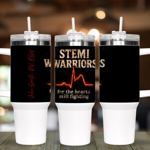 May include: Three white travel mugs with black insulated sleeves. The mugs have white handles and lids with straws. The center mug has the text "STEMI WARRIORS" and a heart rate graphic. The text "for the hearts still fighting" is below the graphic.