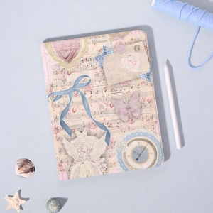 May include: A decorative journal with a musical score design, featuring a light pink cover adorned with floral accents, a blue ribbon, and a butterfly. Additional embellishments include a clock, a cameo, and a vintage letter.