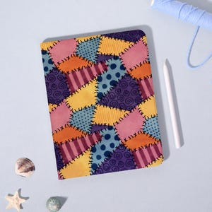 May include: A tablet case with a patchwork design in various colours. The design includes squares and rectangles in shades of pink, orange, yellow, blue, and purple. A white stylus and a spool of blue thread are also visible. The case is approximately 20 cm x 15 cm.