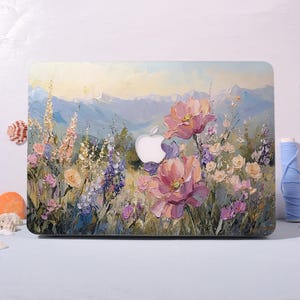 Può includere: Una custodia per laptop con un dipinto floreale. Il design presenta grandi fiori rosa, fiori selvatici viola e una catena montuosa sullo sfondo. La custodia ha un ritaglio per il logo Apple ed è un accessorio protettivo.