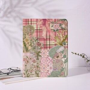 May include: A rectangular notebook with a floral and plaid design. The cover features a collage of pink flowers, green leaves, and a pink bow against a pink and brown plaid background. The notebook is on a white surface.