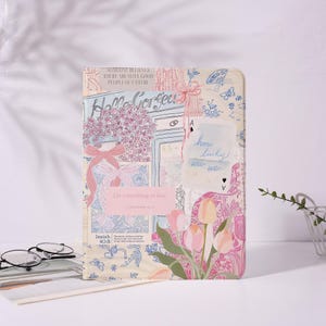 Può includere: Un diario decorativo con un design floreale e testuale. Il diario presenta le frasi "Hello Gorgeous", "Do everything in love" e "How lucky are we". La copertina ha una combinazione di colori rosa e crema con illustrazioni di fiori e farfalle.