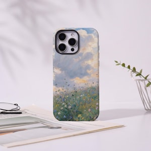 May include: A phone case featuring a landscape painting of a field of wildflowers under a cloudy sky. The case has a black camera module and a smooth finish. The artwork includes shades of blue, green, yellow, and white.