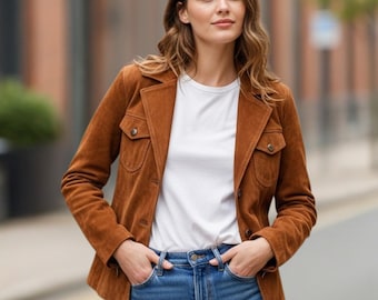 May include: A brown suede jacket with two chest pockets and button closures. The jacket is worn over a white t-shirt and blue jeans. The jacket has a classic, tailored fit.