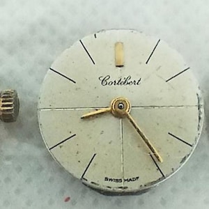 May include: Three vintage watch faces: Omega, Cortébert, and Tissot. Each watch face has a white background with gold-toned hands and markers. The Omega watch face has a gold crown. All three are marked "Swiss Made".