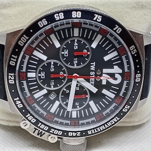 May include: A black and silver TW Steel chronograph watch with a black dial, white numerals, and red accents. The watch features three sub-dials, a tachymeter, and a black leather strap. The watch is displayed on a white surface.