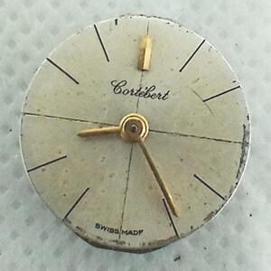 Op de afbeelding: Vintage horlogekast met de merknaam "Cortebert" in cursief schrift. De wijzerplaat is gebroken wit met zwarte uurmarkeringen en goudkleurige wijzers. De woorden "Swiss Made" staan onderaan.