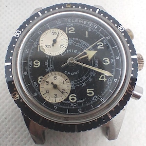 Può includere: Un orologio Cimier Sport vintage con quadrante nero e cassa in acciaio inossidabile. L'orologio presenta una lunetta girevole, due sotto-quadranti e lancette luminose. Il quadrante include il testo "TELEMETRE" e "SWISS MADE".
