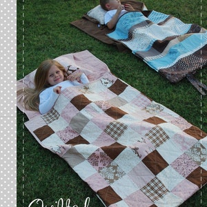 May include: Two children are lying on quilted nap sacks on a grassy surface. The nap sacks are patchwork designs in shades of pink, brown, and blue. The image includes the text "Angela Yosten PATTERNS" and "Quilted NAP SACKS".