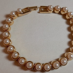 May include: A gold bracelet with a chain of faux pearls. The bracelet is open and ready to be worn.