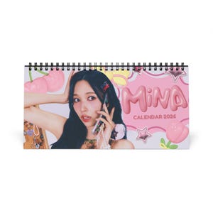 May include: A desktop calendar with a spiral binding. The cover features a woman holding a phone, with the name "MINA" in pink bubble letters and the text "CALENDAR 2026". Pink and white decorative elements are also present.