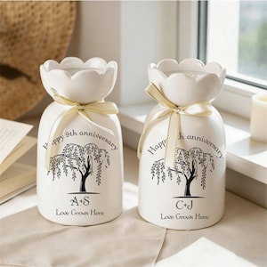 May include: Two white ceramic vases with a scalloped top and tied with a gold ribbon. Each vase has a black tree design and the text "Happy 9th anniversary". One vase has "A+S Love Grows Here" and the other has "C+J Love Grows Here".