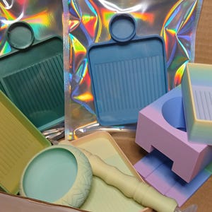 Puede incluir: Un conjunto de cinco bandejas de silicona de colores con diferentes formas y tamaños. Las bandejas están diseñadas para el arte de la resina y la artesanía. Las bandejas son en tonos de verde, azul y morado.